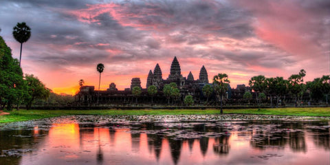 Angkor Wat silhouetted against a pink sunset sky, reflected in a pond