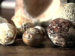 Several small stone spheres on a table, one with a smooth metallic surface and a groove around it