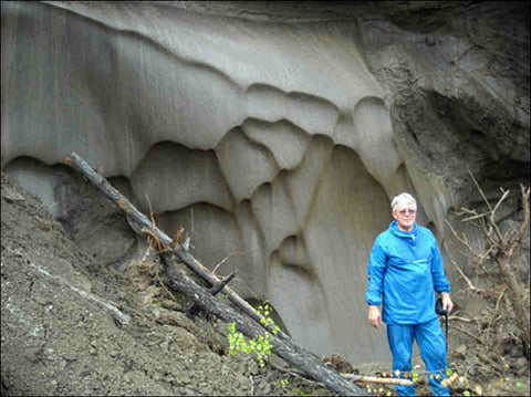 Man in a blue jacket standing beside an exposed wall of frozen permafrost in Siberia