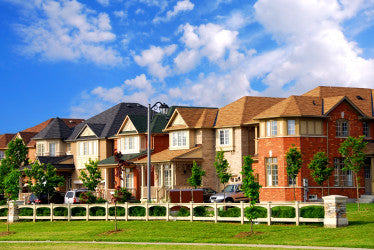 Row of brick suburban houses with front porches and a white fence under a blue sky