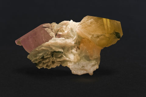 Mineral specimen with a pink crystal and a golden crystal on white matrix, on a dark background