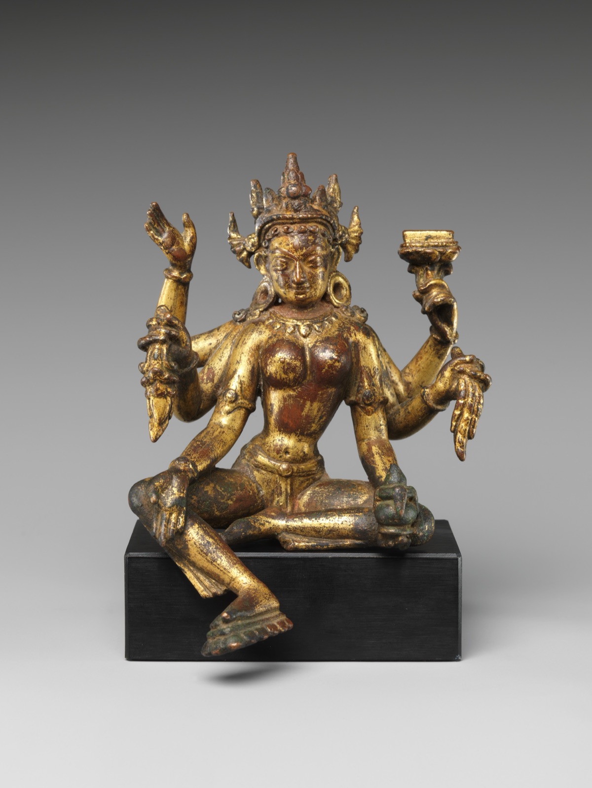 A gilt copper statue of the six-armed goddess Vasudhara, seated with one foot lowered, on a black stand