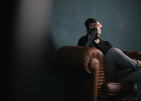 Man sitting on a leather sofa in a dim room, head resting in his hand