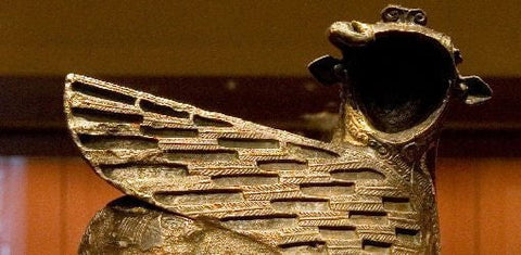 Ancient bronze figure of a winged creature with a feathered wing and an open-mouthed animal head