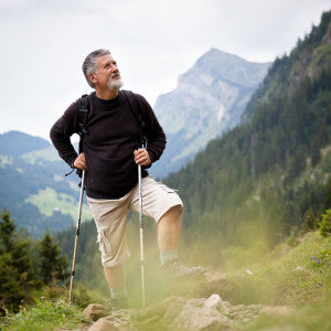 Grey-bearded man hiking a mountain trail with trekking poles and a backpack