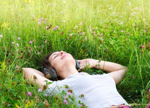 Woman lying in tall grass and clover flowers wearing headphones, eyes closed
