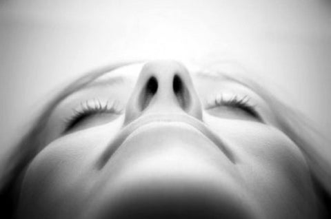 Black-and-white close-up of a face from below, eyes closed, nostrils in focus as if breathing deeply