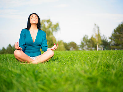 Woman meditating cross-legged on green grass with eyes closed and hands resting on her knees
