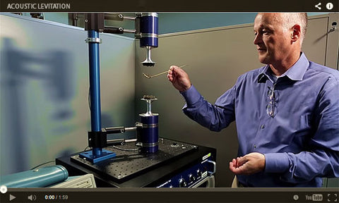 Video still of a man demonstrating acoustic levitation, holding a droplet between two emitters