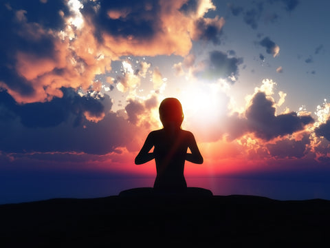 Silhouette of a person meditating cross-legged on a hilltop against a dramatic sunset sky