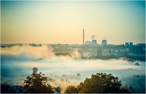 Smokestacks and cooling towers of a power plant above a city covered in low haze