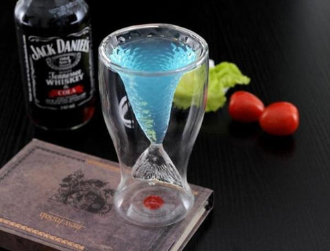Double-walled mermaid tail glass filled with a blue drink, on a book beside a whiskey bottle