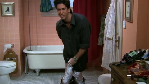 Ross from Friends in a bathroom, struggling to pull on his leather pants