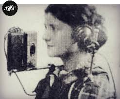 Old photo of a woman wearing a headset at an early telephone, labeled 1881