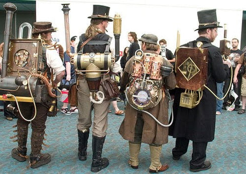 Four people in steampunk costumes with top hats and brass backpack contraptions, seen from behind