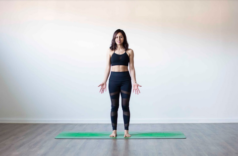 Woman standing in Mountain Pose (Tadasana) on a green yoga mat, palms facing forward