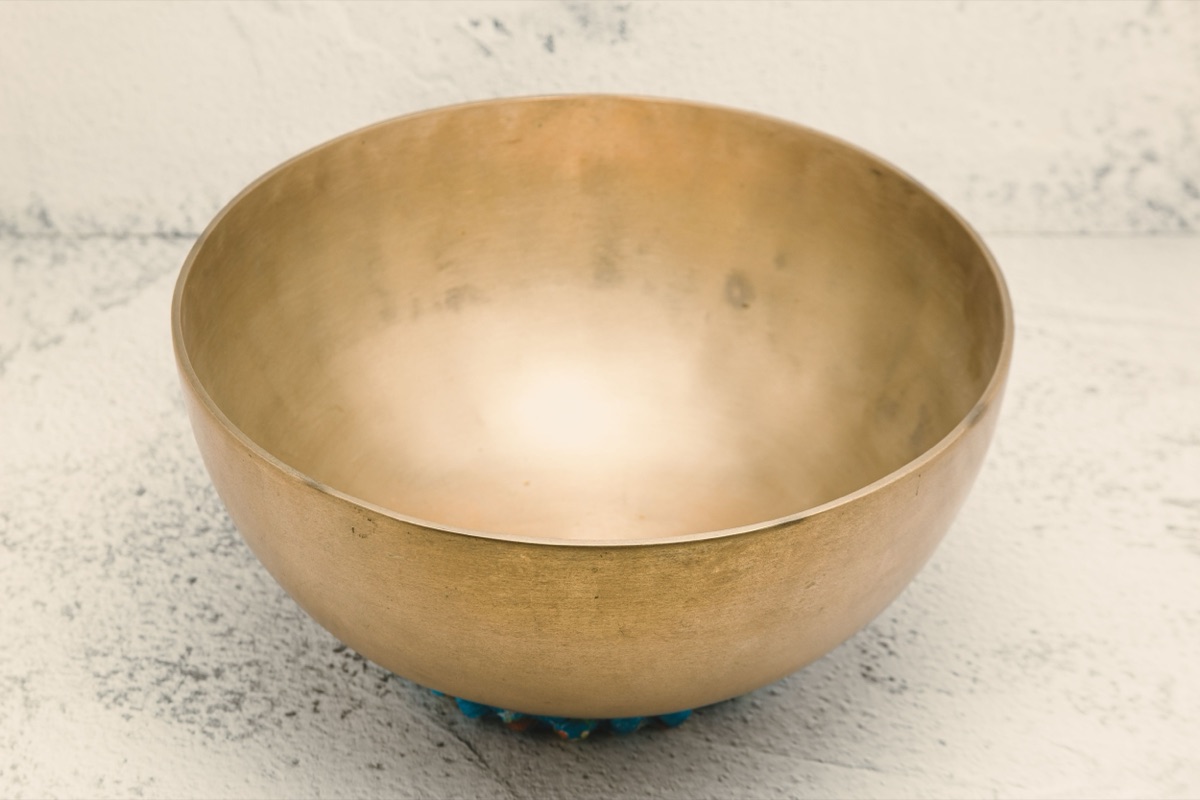 An empty brass singing bowl with a softly worn golden surface, resting on a pale speckled stone surface