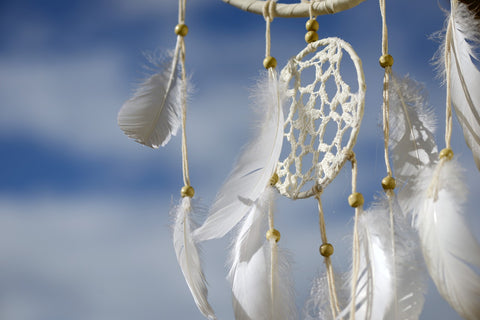 White dreamcatcher with feathers and wooden beads against a blue sky