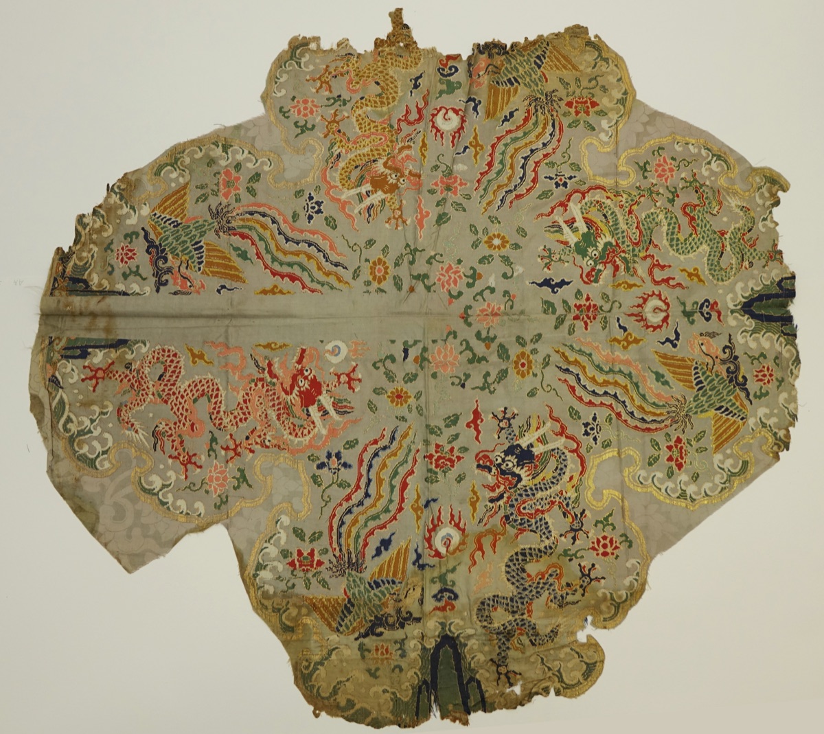 A torn fragment of pale silk brocade woven in red, gold, blue and green with coiled dragons and long-tailed phoenixes among flowers