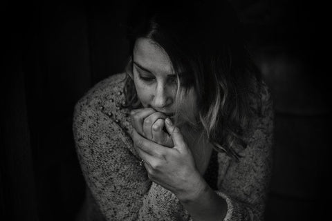 Black-and-white photo of a worried woman in a sweater, hands pressed to her mouth