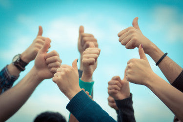 Group of raised hands giving thumbs up against a blue sky