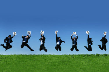 Businesspeople jumping on green grass, each holding a card that together spells SUCCESS