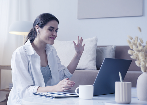 Woman wearing earbuds waving and smiling during a video call on her laptop