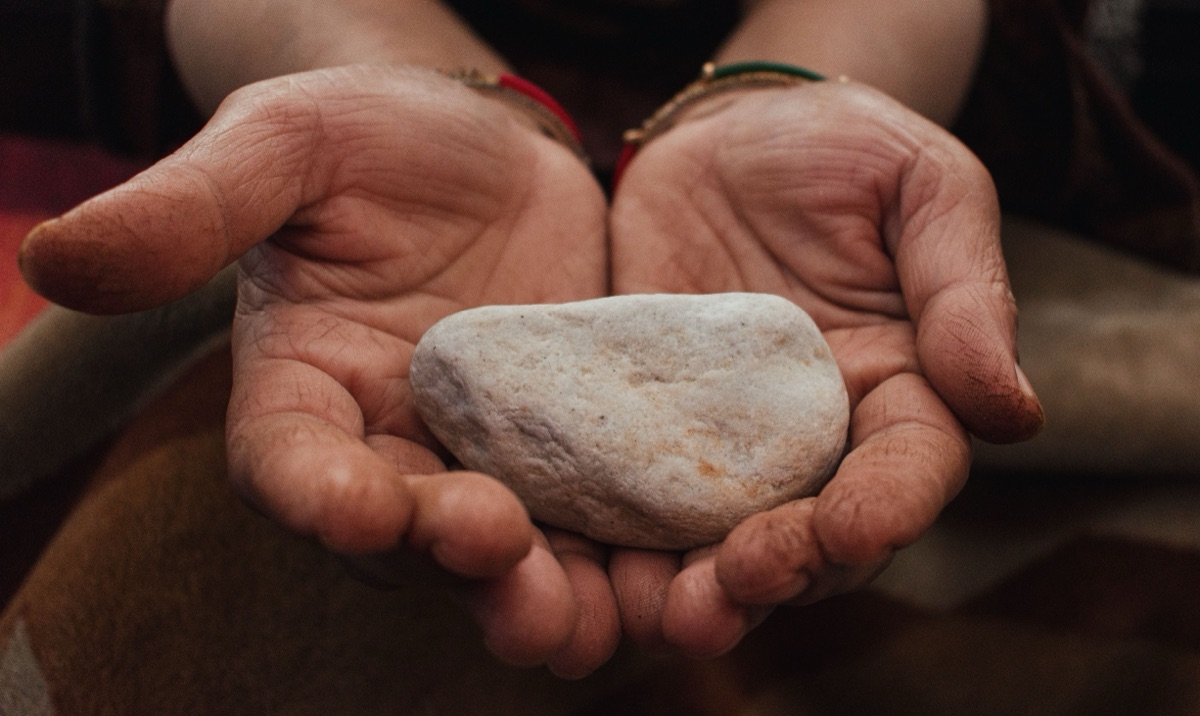 Two cupped hands holding a pale, rounded stone with a grainy surface