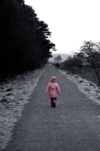 Small child in a pink coat walking alone down a long frosty path lined with trees