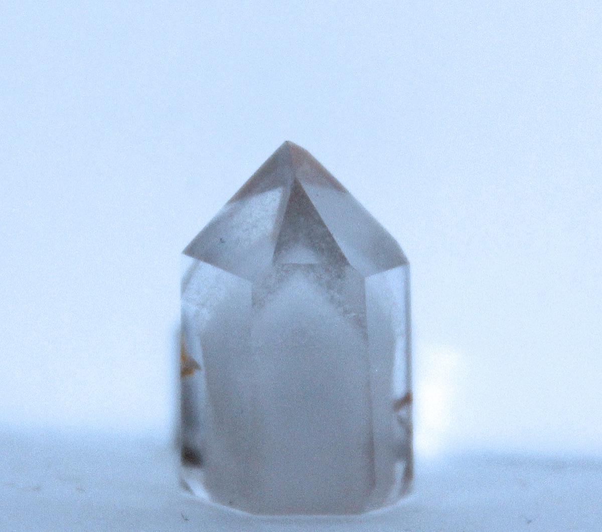 A clear quartz point with a cloudy white inner point inside it, its tip lined up with the outer tip