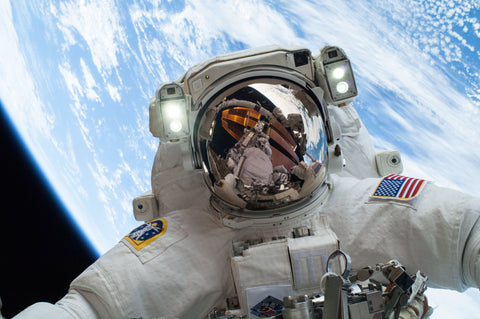 Astronaut in a white spacesuit on a spacewalk above Earth, helmet visor reflecting the station
