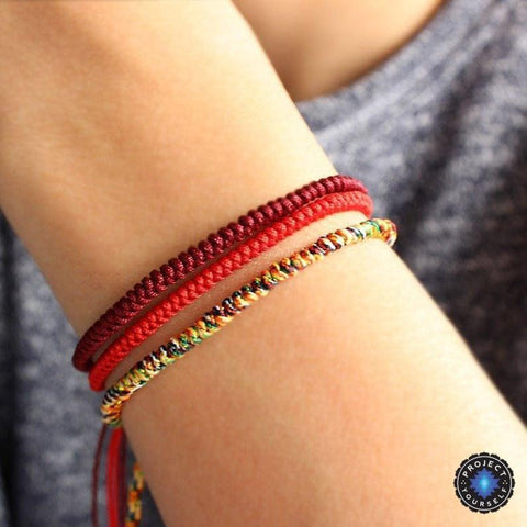 Handmade Buddhist knot rope bracelets in maroon, red and rainbow cord stacked on a wrist