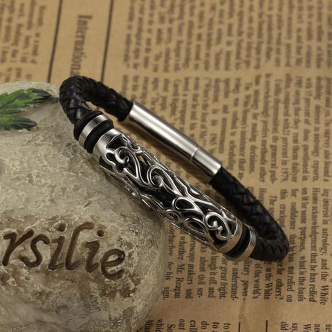 Black braided leather bracelet with a steel clasp and filigree cylinder accent on old newspaper