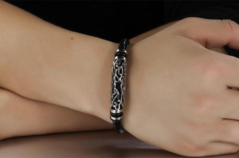 Woven black leather bracelet with a silver tribal hollow cylinder worn on a wrist