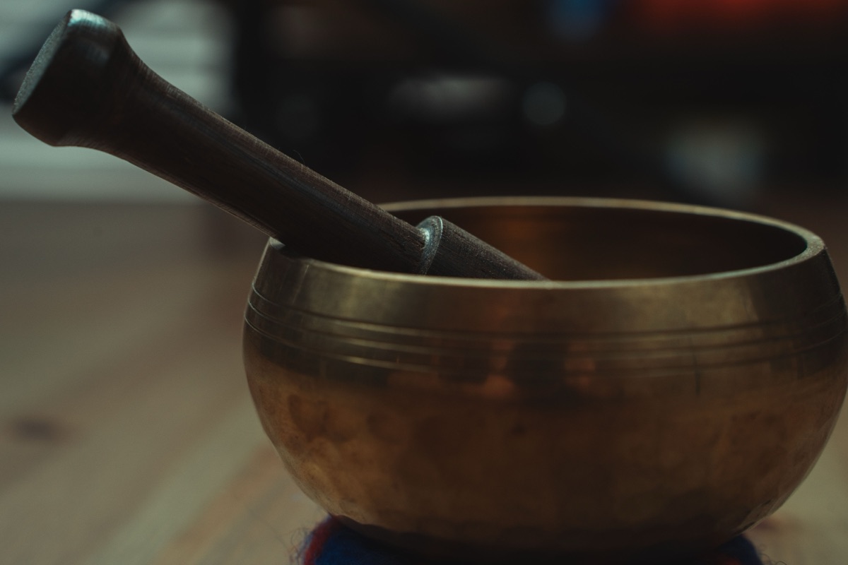 A brass-coloured singing bowl with engraved rings and a wooden striker resting inside it