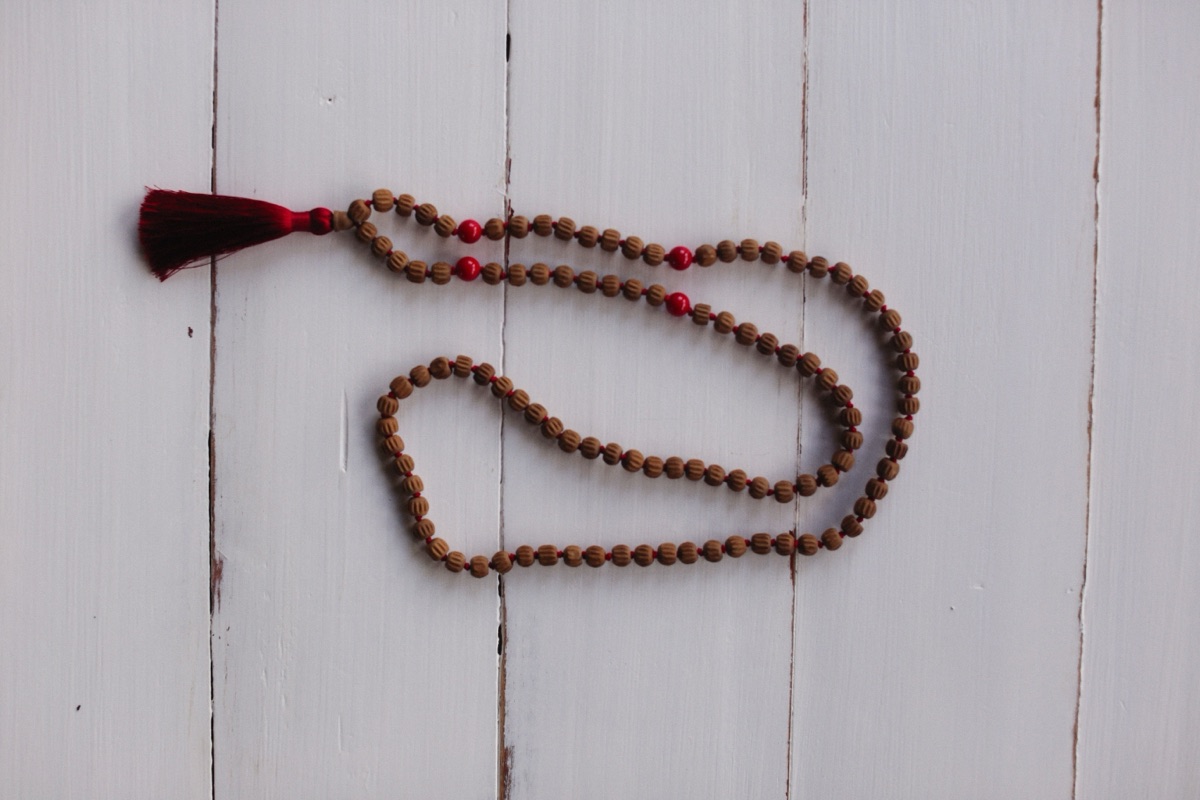 A mala of ridged brown beads with a few red beads and a dark red tassel on white painted boards