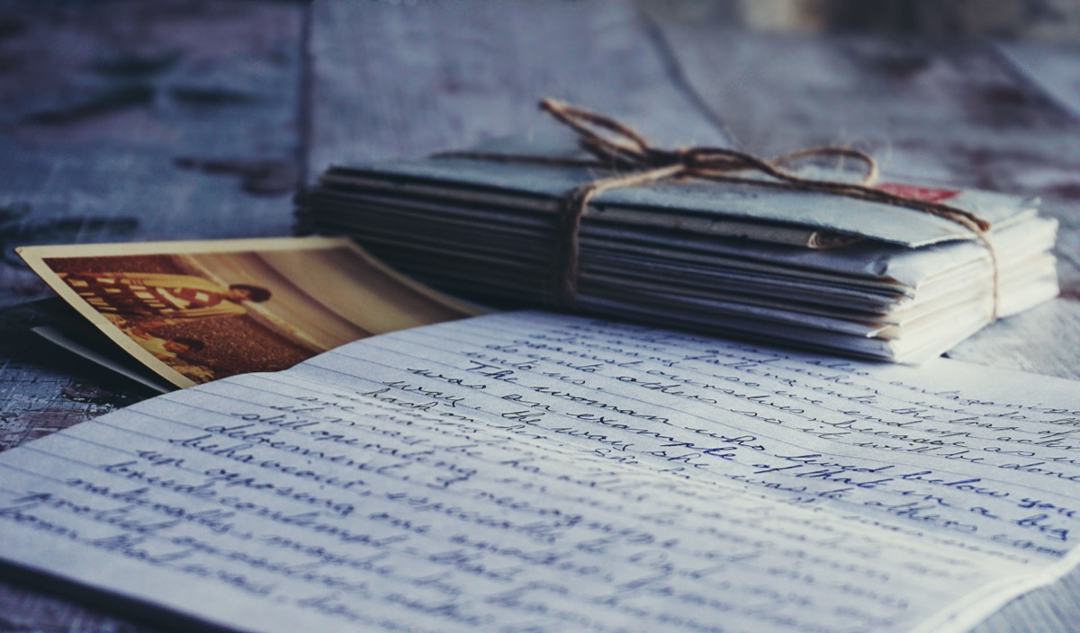 A bundle of old letters tied with string beside a handwritten page and a faded photograph on a wooden table