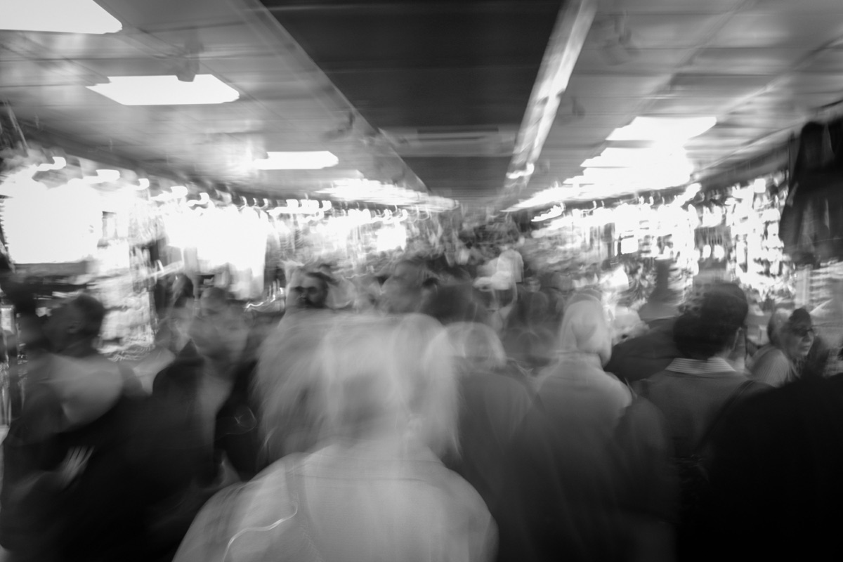 A black and white long exposure of a dense indoor crowd, the people blurred into moving shapes