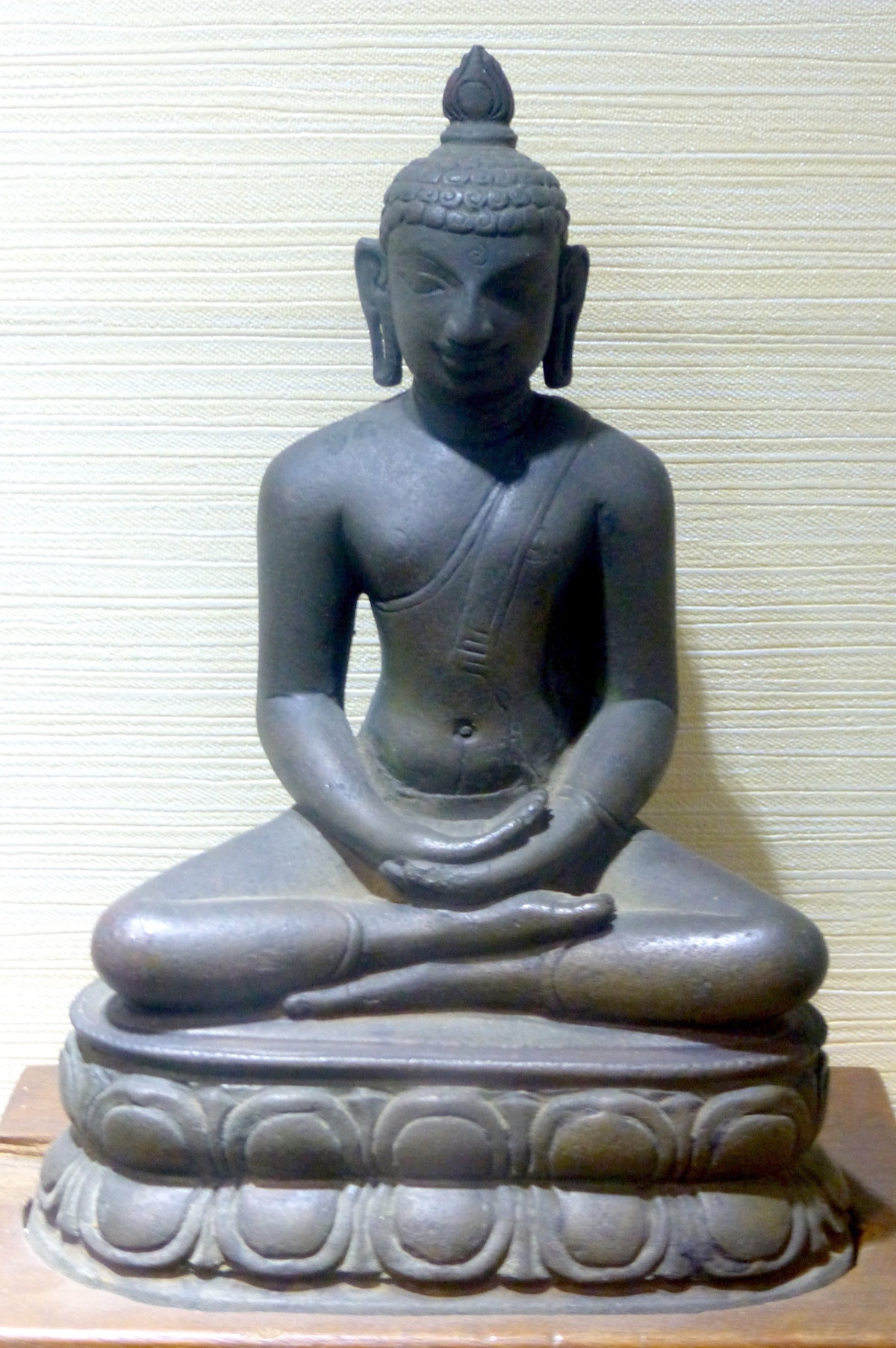 A small dark Buddha statue from Nalanda seated cross-legged on a lotus base, right hand resting on the left in his lap