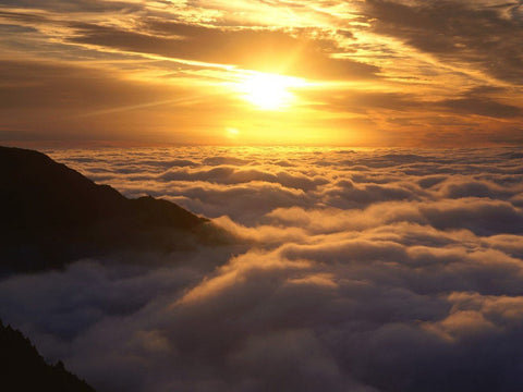 Sun setting over a sea of clouds beside a mountain ridge