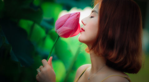 Woman with closed eyes smelling a pink lotus flower bud