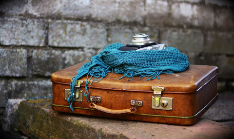 Vintage brown leather suitcase with a teal scarf and a camera on top