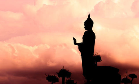 Silhouette of a standing Buddha statue against pink sunset clouds