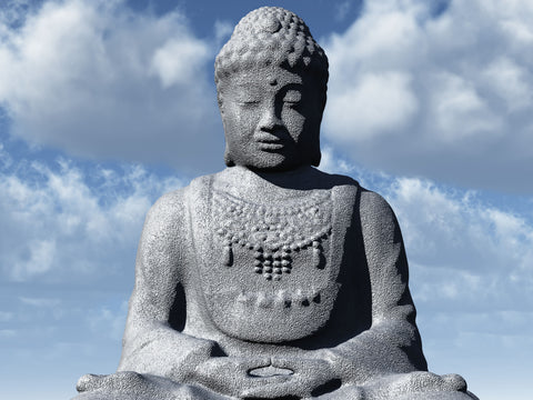 Stone statue of a seated Buddha with closed eyes and a beaded necklace against a blue cloudy sky
