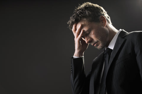 Man in a dark pinstripe suit holding his hand to his forehead with eyes closed