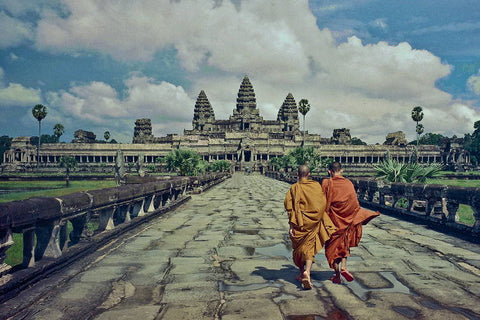 Two monks in orange robes walking the stone causeway toward Angkor Wat