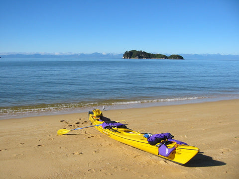 Yellow kayak on a sandy beach facing calm water and a small green island
